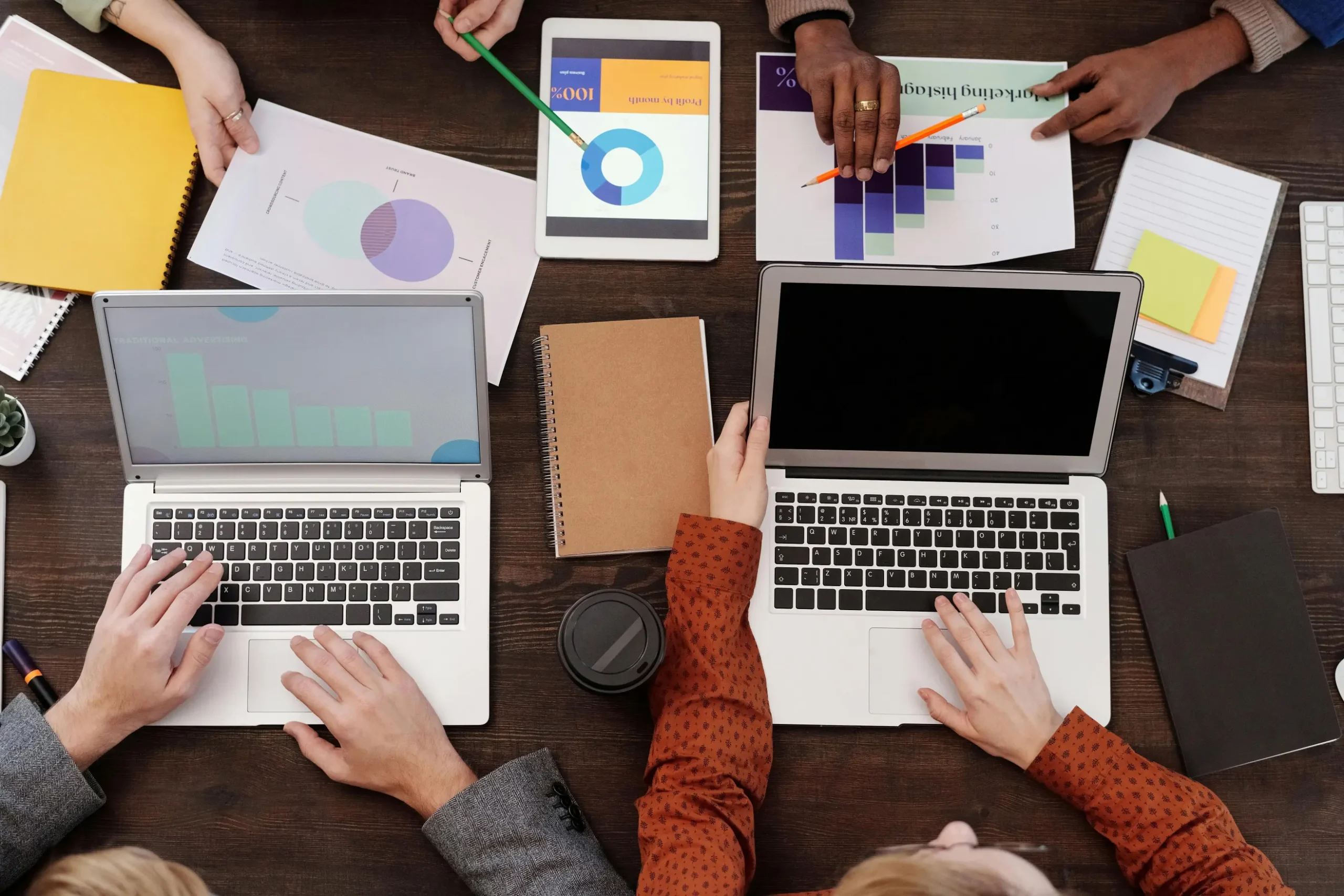 Small business team planning digital marketing strategy with laptops, charts, analytics reports, and tablets